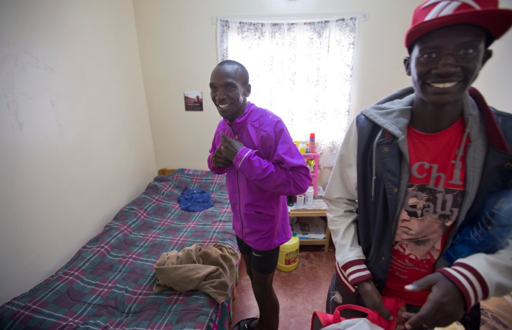 In this Jan. 30, 2016, photo winner of the London, Berlin and Chicago marathons Eliud Kipchoge, left, prepares to change clothes after his morning training run, in the small bedroom he shares with fellow runner Tareq Mubarak Taher, right, who represents Bahrain, at the Global Sports camp near the village of Kaptagat in western Kenya. At the high-altitude training camp in Kenya, star athletes turn their back on modernity and bling for a simple life of hard training and communal, egalitarian living. (AP Photo/Ben Curtis)