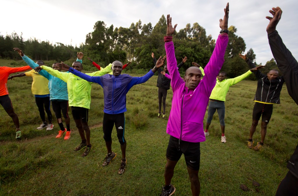 In this Jan. 30, 2016, photo winner of the London, Berlin and Chicago marathons Eliud Kipchoge, center right, stretches with other athletes after their morning training run in Kaptagat Forest in western Kenya. At a high-altitude training camp in Kenya, star athletes turn their back on modernity and bling for a simple life of hard training and communal, egalitarian living. (AP Photo/Ben Curtis)