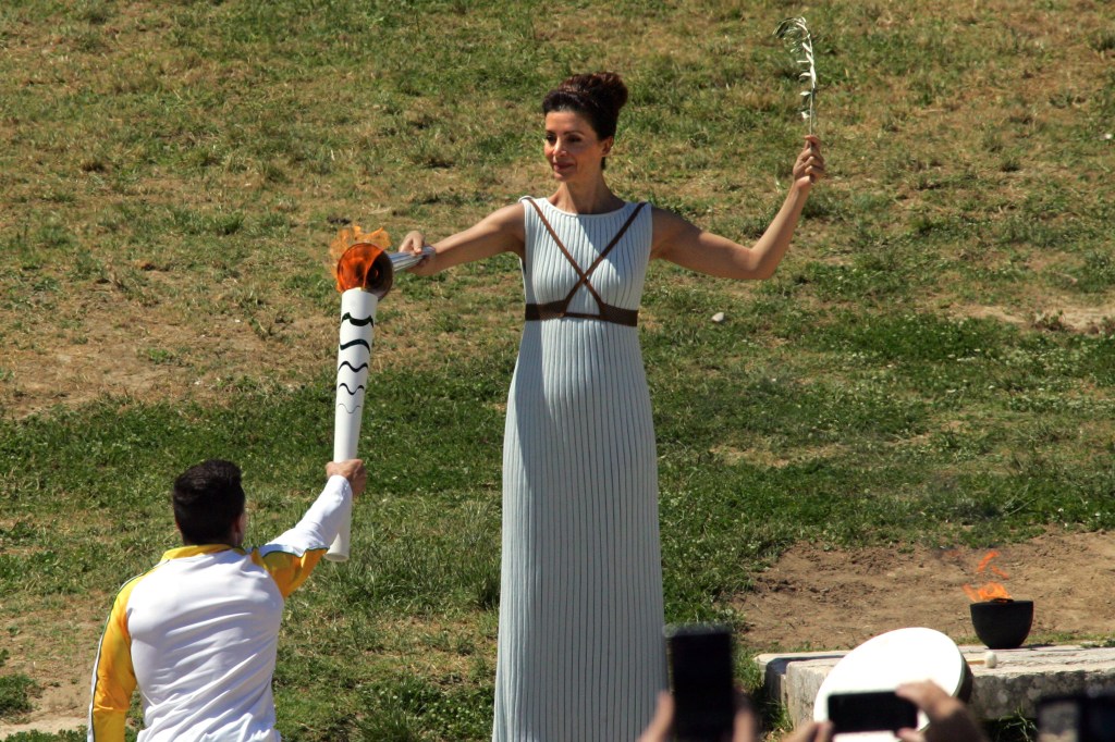 OLYMPIA, GREECE - 21 APRIL: Actress Katerina Lehou who plays the role of high priestess passes the olympic flame to the first torchbearer and reigning world champion gymnast Lefteris Petrounias during the Lighting Ceremony of the Olympic Flame for the Rio Olympic Games on April 21, 2016 in Olympia, Greece. Torchbearers will carry the Olympic Flame from Ancient Olympia on relay through Greece for eight days before a hand-over ceremony at Panathenian Stadium in Athens. (Photo by Milos Bicanski/Getty Images)
