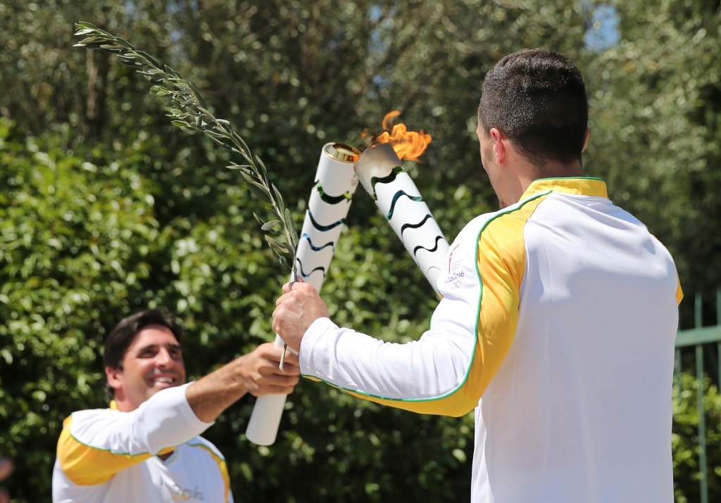 Former Brazilian volleyball player Giovane Gavio, left, receives the Olympic flame by Greek gymnast Eleftherios Petrounias, right, after the ceremonial lighting of the Olympic flame in Ancient Olympia, Greece, Thursday, April 21, 2016. The flame will be transported by torch relay to the Brazilian city of Rio de Janeiro, which will host the 2016 Olympic Games. (AP Photo/Petros Giannakouris)