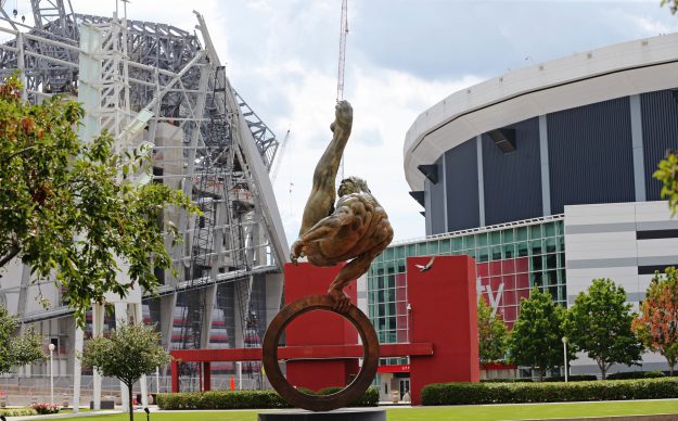 In this Monday, July 18, 2016 photo, a statue of a gymnast stands between the Georgia Dome, right, home of the 1996 Summer Olympic Games gymnastics and basketball events and current home of the Atlanta Falcons football team, and the Falcons' new stadium under construction at left. A divider transformed the Georgia Dome, a 70,000-seat football stadium into two separate arenas, one the site of second Olympic Dream Team winning gold in men's basketball, the other where the Magnificent Seven captured America's first victory in women's team gymnastics. Just 25 years after its opening, the dome is slated for demolition after $1.4 billion Mercedes-Benz Stadium opens next door in 2017. (AP Photo/John Bazemore)