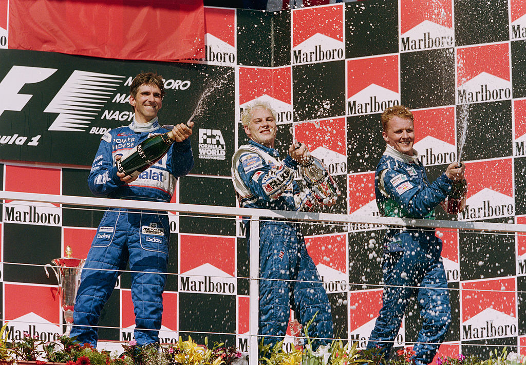 Jacques Villeneuve (C) of Canada sprays champagne to celebrate with second placed Damon Hill (L) and third placed Johnny Herbert after winning the Hungarian Grand Prix on 10th August 1997 at the Hungaroring Circuit, Budapest, Hungary. (Photo by Mark Thompson/Getty Images)